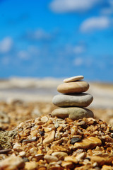 Stone pyramid on shore on blurred blue background. Balance symbol. Vertical backdrop with copy space