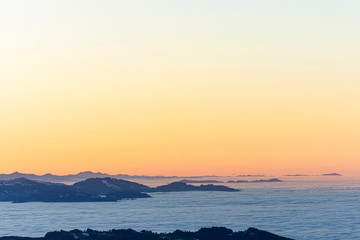 Fototapeta premium Colorful sunset at the edge of the Alps with snow-covered, forested hills. Fog over the Rhine valley and the lowlands. Austria, Switzerland. Lots of copy space