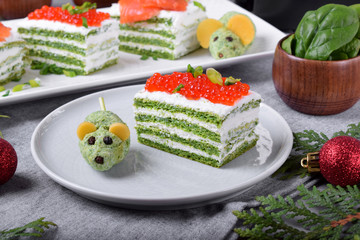 Layered salty cake with spinach, cream cheese and red caviar and a mouse shaped appetizer next to it on the ceramic plate