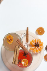Drink red and yellow in glass goblets. Anise stars float in it. Next to the linen fabric is peeled mandarin, dried mandarin rings, cinnamon sticks and anise stars.