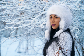 Girl in warm hat on background of trees with snow.