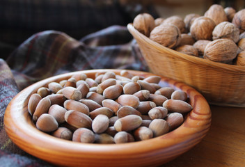 A bowl full of hazel nuts with a basket full of walnuts, in close up with a rustic brown plaid background. Naturel health food.