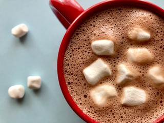 top view of hot cocoa with marshmallows in a red mug on a light blue background