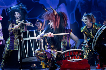 Fototapeta na wymiar Traditional Japanese performance. Taiko drummers in a wigs and a demon masks perform on stage with drum on a dark background. Demons from Japanese mythology.