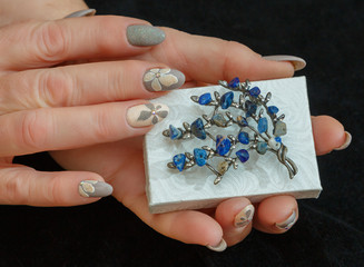 Female hands with a multicolored manicure and a brooch with blue stones closeup
