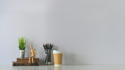 Decorative workspace with books, dummy model, coffee, pencil and house plant on white table.