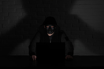 Hacker in black mask and hood at the table