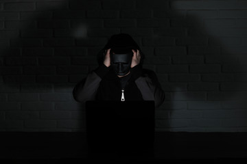 Hacker in black mask and hood at the table
