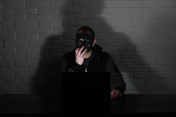 Hacker in black mask and hood at the table