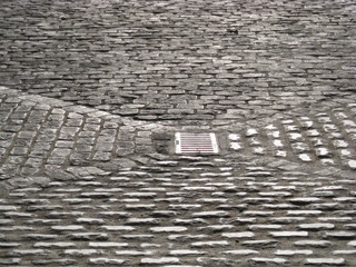 Patio de adoquines antiguo con alcantarilla en centro para  canalizar aguas, pavimento gris en...