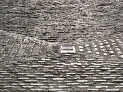 Patio de adoquines antiguo con alcantarilla en centro para  canalizar aguas, pavimento gris en vertientes inclinadas en forma de tri&aacute;ngulos