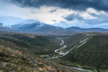 Cairngorms mountain seen in the evening light show a stream in the valley  with water, snow and heavy blue clouds.