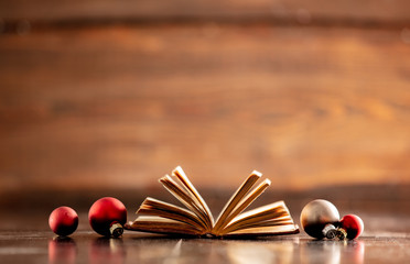 Old book and Christmas baubles on wooden table