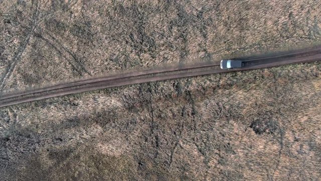 SUV black crossover car traveling on countryside road top aerial view. Off road car driving on dirt road through countryside field in village. 