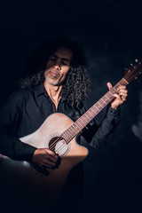 Obraz premium In dark photo studio curly middle aged man is posing with guitar for photographer.