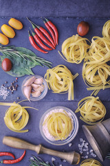 Pasta on the table with spices and vegetables. Noodles with vegetables for cooking on a black stone background.
