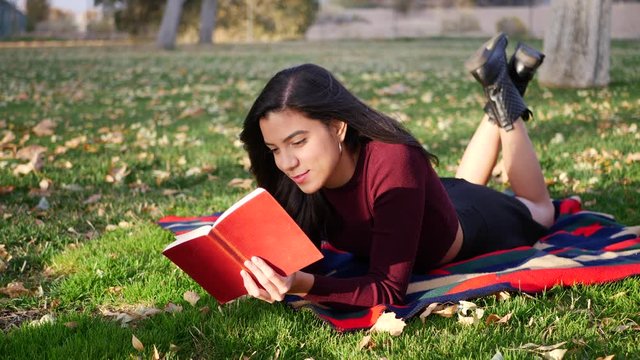 A cute young woman college student reading a book outdoors in the park before class starts in the fall semester.