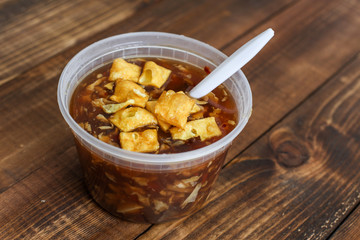 Hot and sour soup in plastic tray with spoon inside