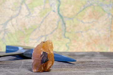The geologist's hammer and mineral are laid out on a wooden table against a topographic map. Background