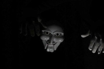 White scary mask on a black background with whites hand.