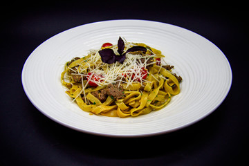 Pasta with beef and cherry tomatoes on black background
