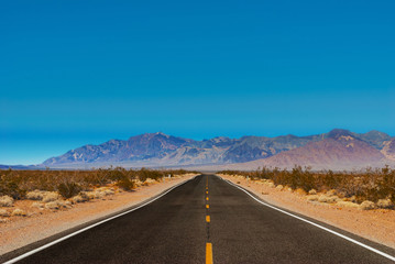 The road passing through the desert against the backdrop of mountains.