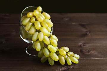 Green, ripe, juicy grapes are placed in a glass vase, which stands on a dark wooden background of boards.