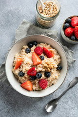 Bowl of oatmeal porridge with fresh berries blueberry strawberry and raspberry. Table top view shot, concrete or cement background