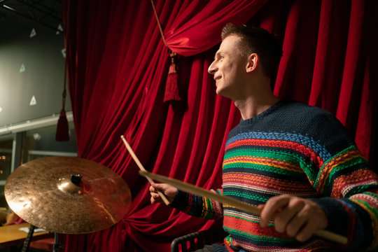 handsome young guy playing drums on stage. against the background of the red curtain