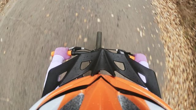 Pov view. One caucasian children rides bike road in autumn park. Little girl riding black orange mtb cycle in forest. Kid goes do bicycle sports. Biker motion ride with backpack and helmet.