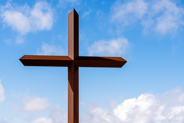 Steel cross against background of cloudy blue sky at Saint Anthony Greek Orthodox Monastery in Florence, Arizona.