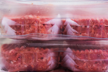 Stacked grass fed organic raw beef burgers layered between wax paper in plastic containers. Preparing barbeque grill meal