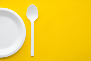 Plastic white spoon and plate on yellow background. Cooking utensil. Top view. Minimalist Style. Copy, empty space for text