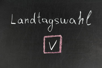 Chalkboard with a hand writing Landtagswahl in german with a checkbox, translate federal election