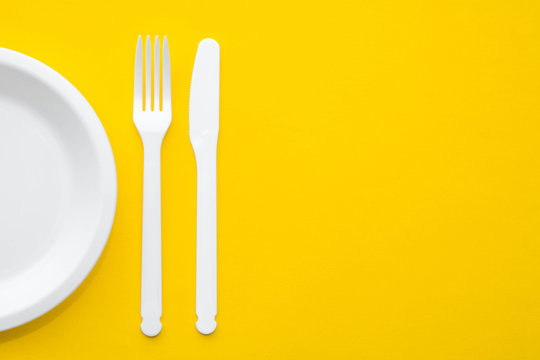 Plastic white fork, knife and plate on yellow background. Cooking utensil. Top view. Minimalist Style. Copy, empty space for text