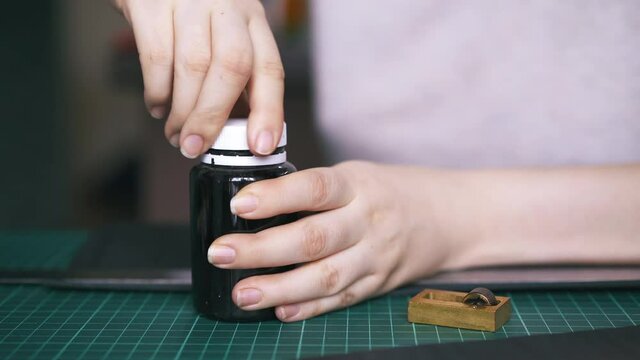 CU: Careful woman closes leather paint bottle and takes pure copper on green cushion board close view