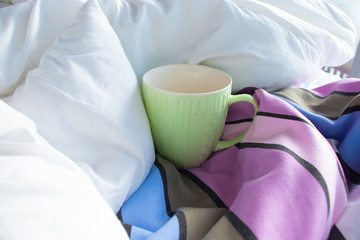 Fototapeta na wymiar Green cup in bed with white blanket and striped duvet