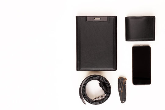 Men's set. Black leather diary, black leather belt, black leather wallet, smart watch, smartphone and knife on a white background. View from above. Copy space.