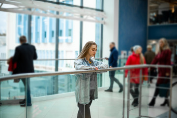 Teenager. Young pretty white caucasian teenage girl with long hair with problem skin and long hair in a shopping center near the railing.