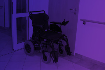 lonely black wheelchair stands empty against a wall