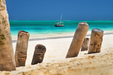 Fototapeta na wymiar view through old wooden trunks on the beach to fishing boat in water on Zanzibar island in Tanzania