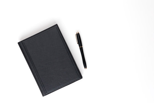 Flat lay. Black leather diary and black pen on a white background. View from above.