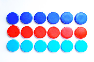 Plastic multi-colored bottle caps are arranged in three rows on a white background. Close-up.