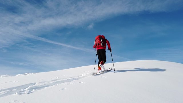 Ski Mountaineer climbs a snowy mountain over blue clear sky. Winter season, sunny day. Concepts: achieve a personal goal, exploration, new horizons.