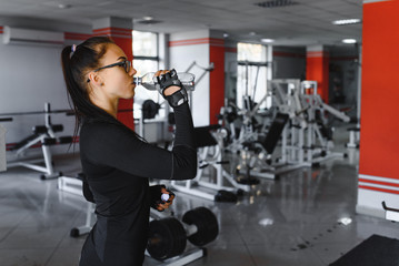 Young woman drinking water after exercising. Fitness gym.