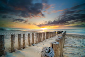 Groynes and wave breakers in a smooth sea just before sunset at a Dutch coast
