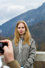 Blonde hipster girl posing in front of smart phone in men hands on the background of mountains. Autumn in Montenegro, partial defocus.