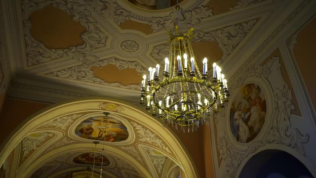 Gorgeous golden chandelier in a Renaissance church with paintings and bas-reliefs. Pan left, truck right.