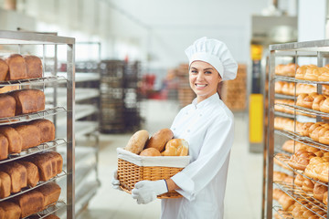 A baker woman holding a basket of baked in her hands at the bakery