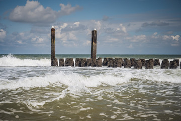 Splashing waves of the North Sea on the wooden breakwaters of the Dutch coast